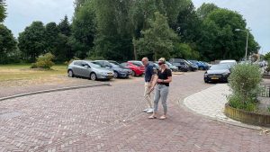 Een vrouw met een slecht zicht bril en een witte taststok steekt de straat over. Ze wordt begeleid door een man die naast haar loopt.