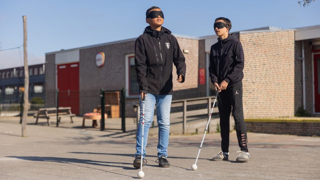 Twee jongens met een blinddoek en een taststok op het schoolplein
