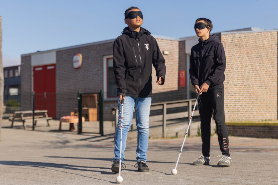 Twee jongens met een blinddoek en een taststok op het schoolplein