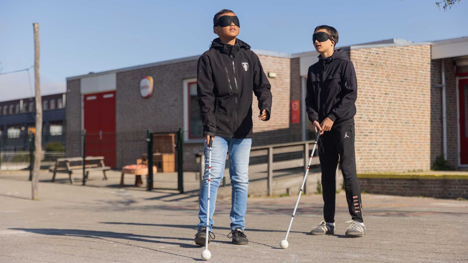 Twee jongens met een blinddoek en een taststok op het schoolplein Twee jongens met een blinddoek en een taststok op het schoolplein